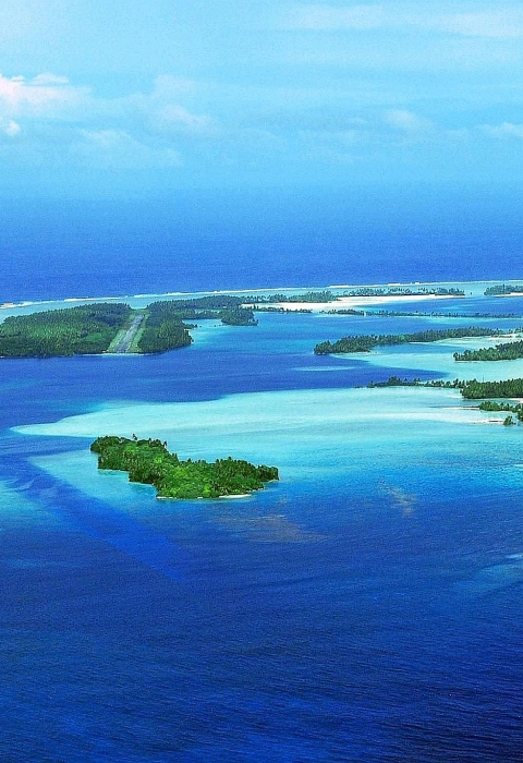 Aerial view of an island atoll surrounded by sandy reef in the deep blue ocean