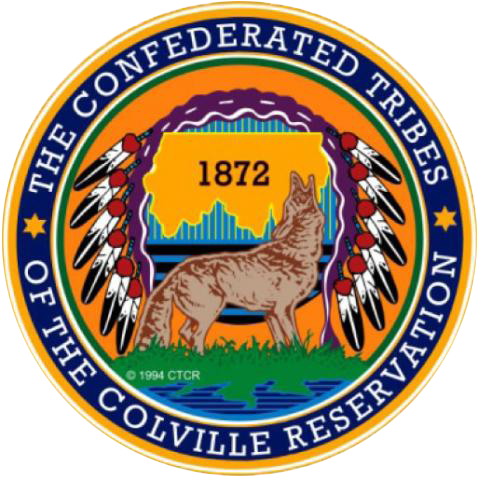 Round seal with yellow-orange background, title around the edge, and in center, a howling wolf, the outline of the reservation with the date "1872," and an eagle headdress