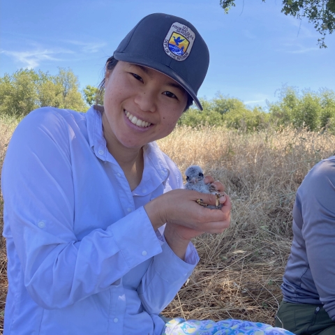 a woman smiles outside while holding a chick in her hands