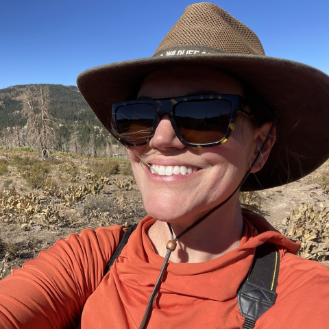 a selfie of a person wearing a brown sunhat, sunglasses and an orange shirt