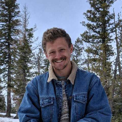 a man with a mustache stands in a pine forest