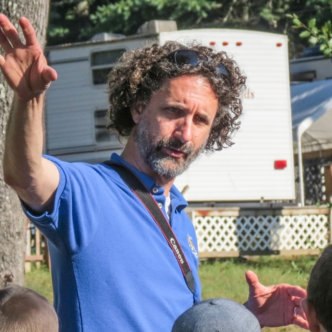 Male biologist standing before students, hand raised in the air