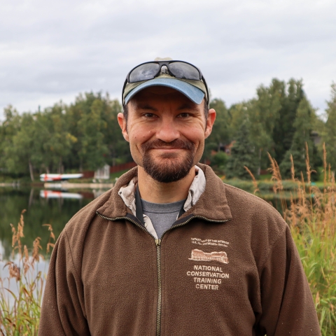 Man with beard and baseball hat wearing a brown National Conservation Training Center jacket