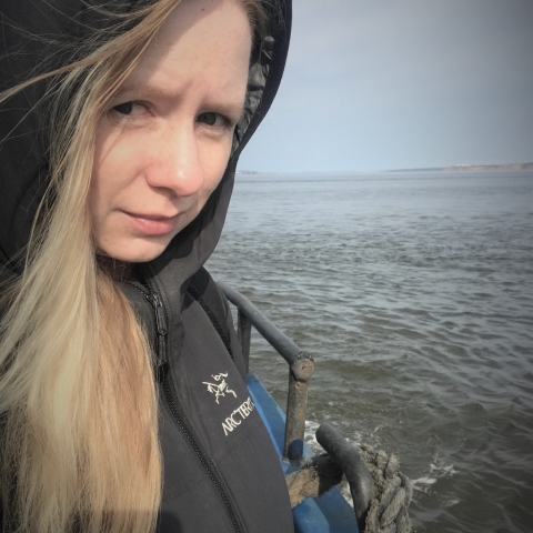 A close-up of a woman standing on a boat with water and sky behind her