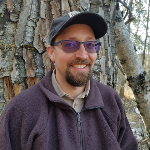 man in brown jacket stands near a tree