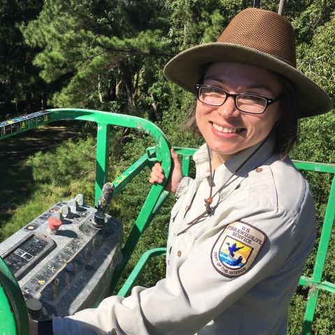 Woman smiling at camera standing up high in bucket truck.