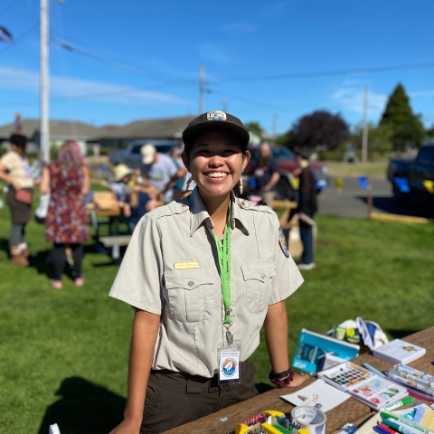 USFWS Staff Karen Ceballos wearing a USFWS official uniform and standing at a craft table at an outdoor festival.