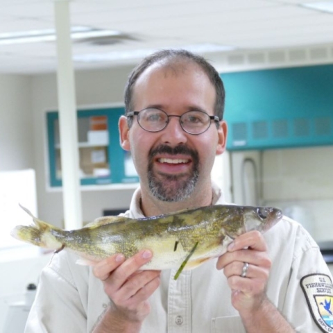 Man smiles whie holding up fish in a lab