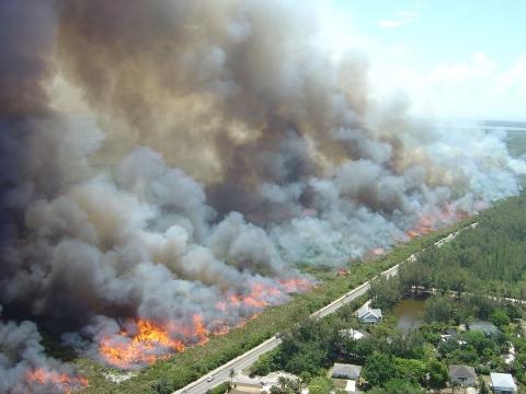 A huge smoke plume moves away from a housing development right next to a road