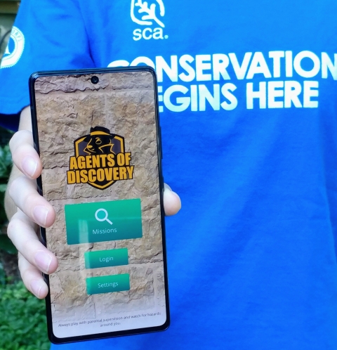 An intern holds a phone with the Agents of Discovery home screen open