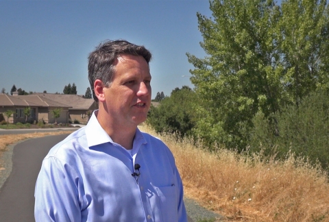 A man outside with trees and homes in the background.