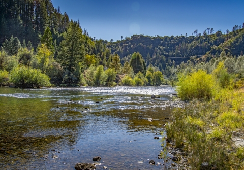 a landscape of a river with tree covered hills in the background