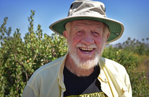 Man with white beard in a sun hat smiles at camera