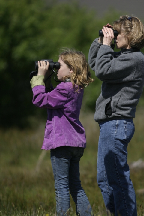 A woman and a young girl look through binoculars into the distance