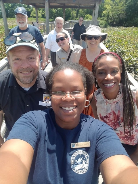 A smiling woman in a navy tee-shirt in foreground poses for a photo with several other people behind her.