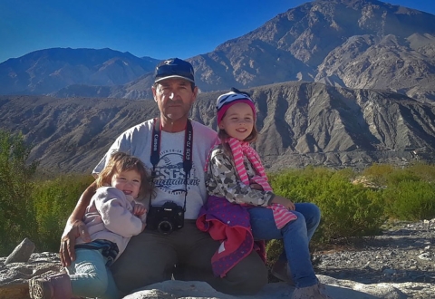 Man sits on rock with a small girl on either side