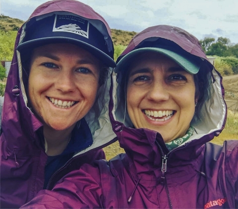 Two women smiling and wearing purple raincoats