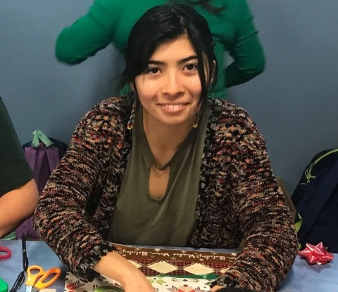 A smiling young woman looks up at camera from an art project.