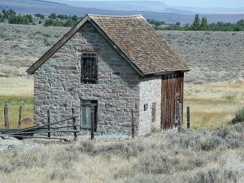 A small stone, structure in a dry, rolling meadow with mountains in the background