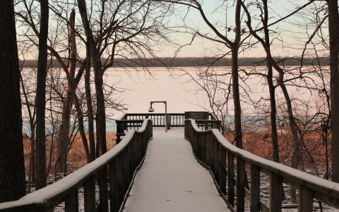 pink hued snow covers a board walk lead to platform at the edge of a frozen lake 