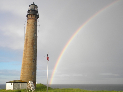 a rainbow touches the ground below a towering lighthosue