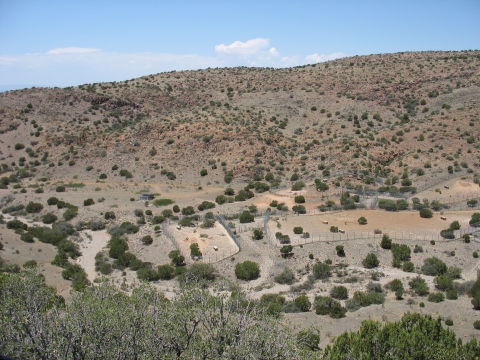 A photo looking out onto a desert valley with large fenced enclosures. There are hills in the background with low vegetation. 