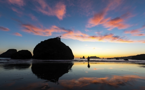 a colorful sunset at the ocean with a man walking in the distance.