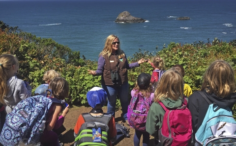 a woman talking to children with water behind her