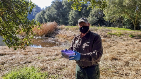 A man with a mask on outside holding a small container.