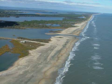 Aerial view of thin coastal barrier with ocean breach.