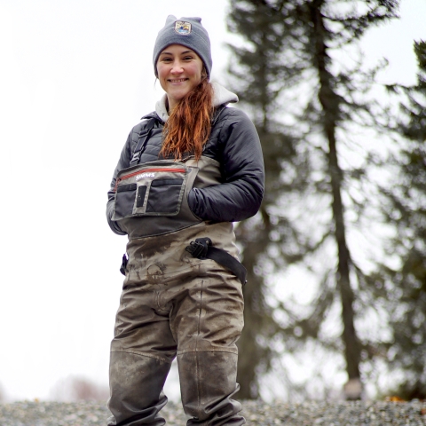 woman in waders with brown hair and trees in the background