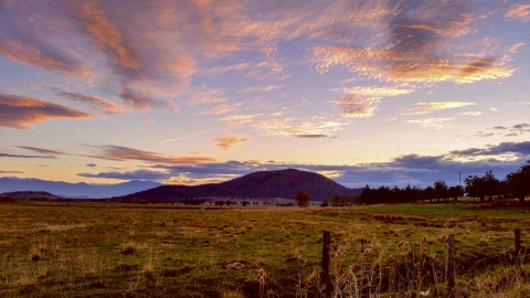 a sunset showing a small hill and a field of grass