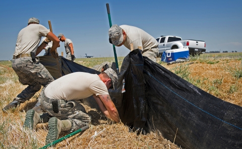 Military soldiers install black fabric fencing in a dry field to stop salamanders from crossing into the air force runway