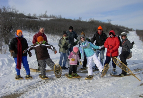 11 people in snowshoeing gear posing happily on a snowy trail