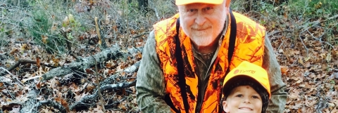 A grandfather and his grandson in hunting gear in a leafy autumn setting