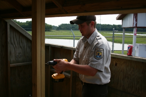 A person using a drill on a wooden photo blind.