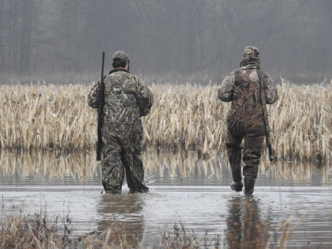 Two hunters in camo walking through water.