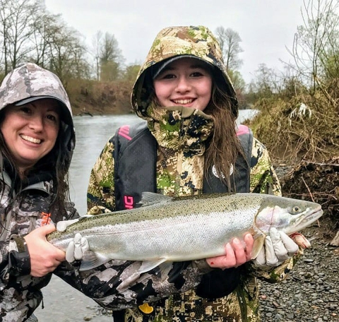 Young girl smiling and holding a fish next to a river