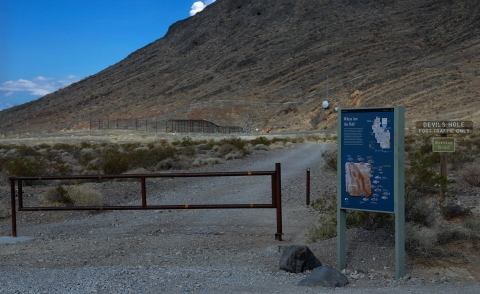 Interpretive sign next to a gate, a rocky hill is in the background