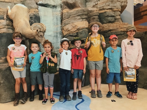 A group of youth standing in front of a faux rock wall. Some of the kids hold blue pastic badges