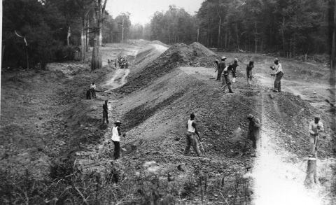 Black and white photo of many African American men building up a large pile or soil using hand tools