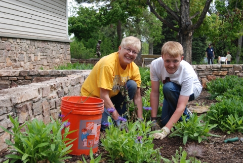 Two volunteers kneel in a garden to plant flowers.