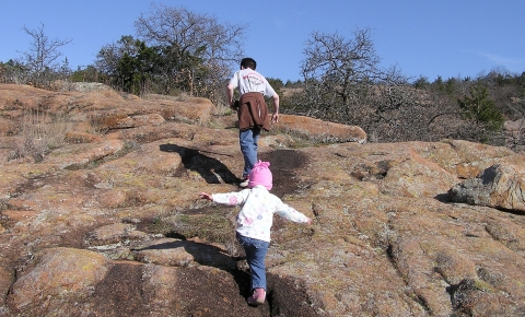 A young child following an adult up a wide, rocky trail