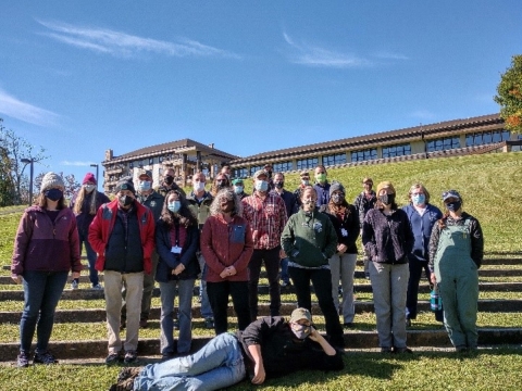 A group of people gathered outdoors standing in front of a fence wearing masks