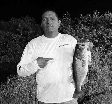 A man pointing a finger with one hand at a fish he caught and is holding by the head with the other hand. 