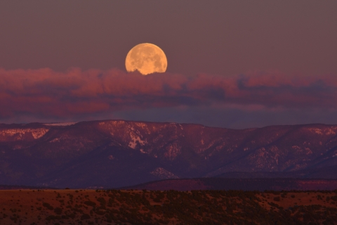 The moon -- brilliant but slightly obscured by clouds -- over a mountain range near dawn