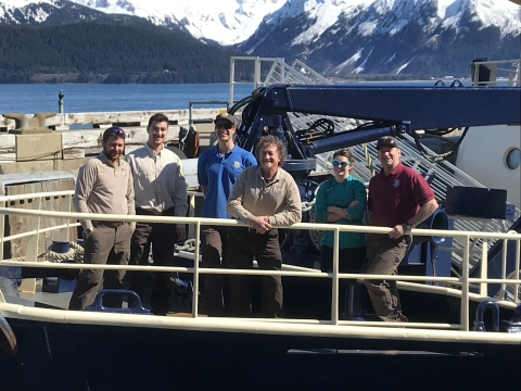 Crew of 6 people stand on deck of ship.