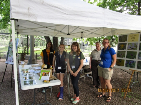 2 adults and 3 youth tabling under a white tent 