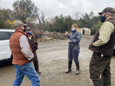 Four people stand in a circle. They are all wearing face masks and one woman appears to be gesturing to the right with her hands. 