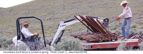 Two men using a front-end loader to move pipes for fencing